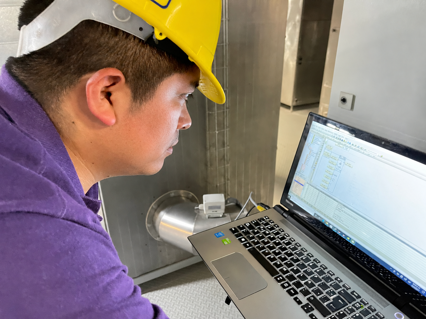 Ingeniero de DGM con casco programando un PLC desde una computadora en planta